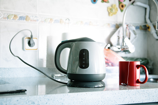 A modern electric kettle in a kitchen, and a red tea cup