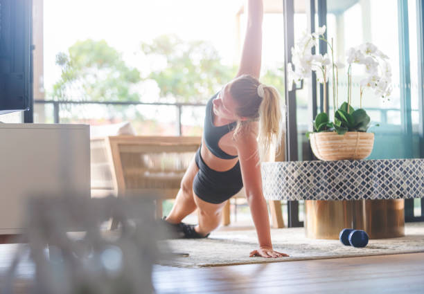 Young woman exercising at home. Young woman exercising at home. She is lying down doing stretching exercises with some weights. She is on the rug in the living room with a balcony in the background sports training australia stock pictures, royalty-free photos & images