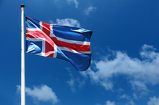 National Flag of Iceland. Image for Icelandic Republic Day, National Day. Flag of Iceland on a high flagpole. Waving Icelandic Flag Against a Blue Sky with Clouds.