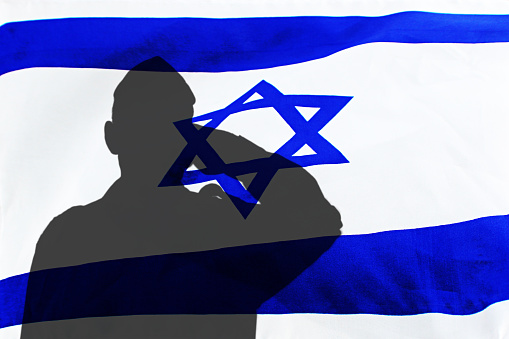Silhouette of an Israeli soldier giving salute on a background flag of Israel. Concept: IDF, patriotism in Israel.