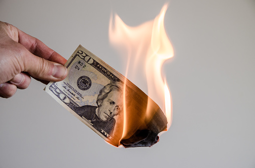 Hand holding a burning twenty US dollar bill on a white background