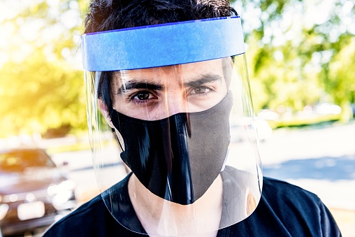 Hispanic Young man posing with a protective mask and plastic face shield because Covid-19 pandemic