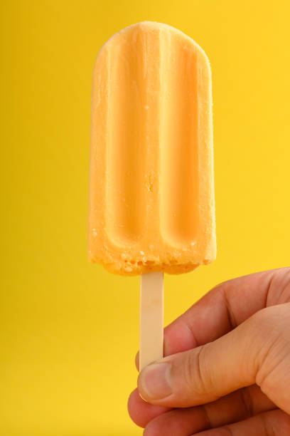 istock hand holding a mango pudding flavor popsicle on a yellow background 1226318556