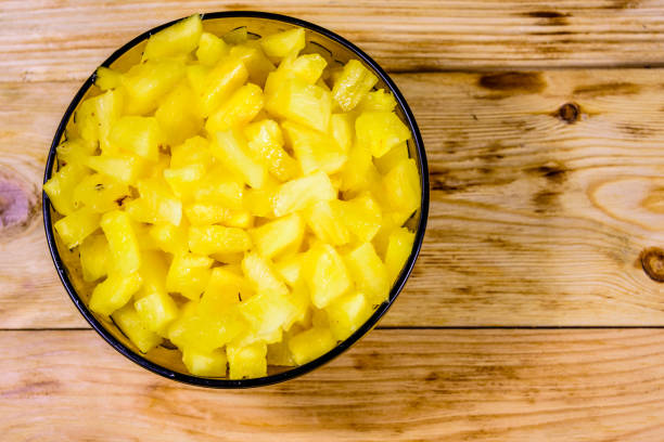 istock Glass bowl with chopped pineapple on wooden table. Top view 1226320056