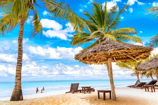 Tumbonas bajo sombrilla y palmeras en la playa de arena junto al océano y el cielo nublado. Antecedentes vacacionales. Idílico paisaje de playa en la playa de Diani, Kenia, Africa photo