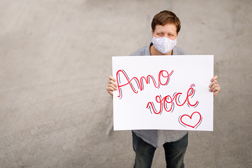 Man holding a love you poster wearing homemade mask.