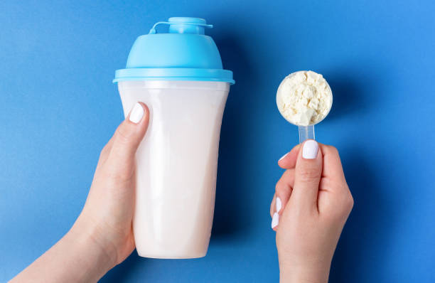 female hands with white manicure hold bottle of protein shake and a measuring spoon with protein powder, top view - protein powder imagens e fotografias de stock