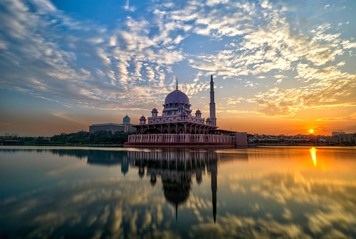 Sunrise with nice clouds against a mosque with water reflection