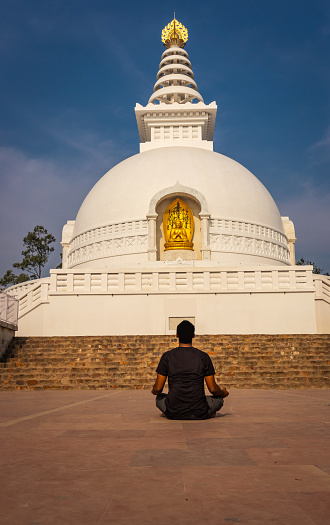 monk praying at buddhist stupa isolated with amazing blue sky from unique perspective image is taken at Vishwa Shanti Stupa Rajgir in Bihar india. This stupa is symbol of world peace.
