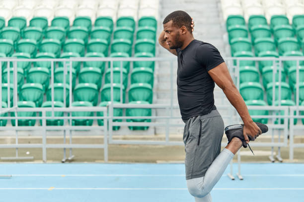 motivated strong man stetching his legs, warming up before training motivated strong man stetching his legs, warming up before training, side view close up portrait. green seats in the background of the photo.health, body care knee to the head pose stock pictures, royalty-free photos & images