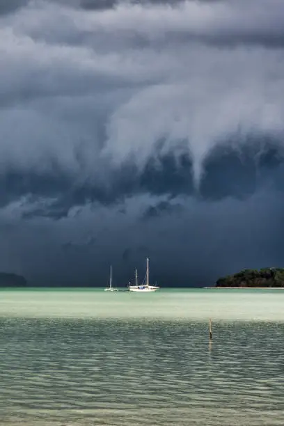 Extreme weather dark Virga thunder clouds with torrential rain are forming above the sea.  Below is a small, white sailboat.  These weather events are also known as tornado, cyclone or hurricane, are unfortunately becoming more common around the world due to Global Warming and Climate Change.  These weather patterns are violent and dangerous, often claiming numerous lives in the areas which they occur.  Location is Andaman sea, Thailand.