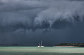 Foreboding extreme weather cyclone clouds forming at sea above small white sailing boat
