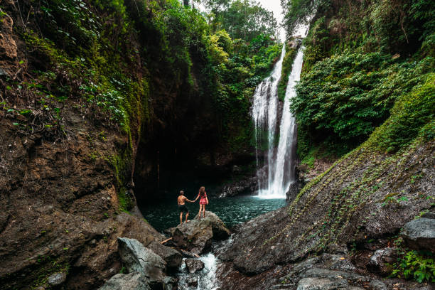 amantes na cachoeira, vista para trás. casal admirando uma linda cachoeira na indonésia. casal de férias em bali. viagem de lua-de-mel. o casal está viajando pela ásia. férias na ilha de bali - romance honeymoon couple vacations - fotografias e filmes do acervo