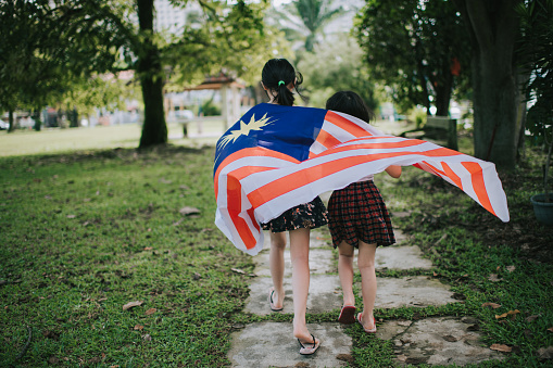 an asian chinese sisters running in the public park with malaysia national flag happily
