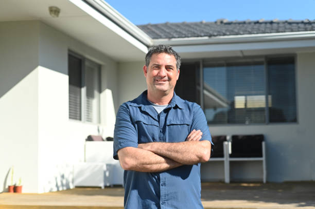 happy adult man standing in front of his new home - reduction looking at camera finance business imagens e fotografias de stock