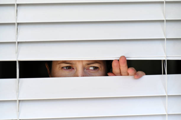 suspicious adult woman looking outside home window - peeking analyzing staring watching imagens e fotografias de stock