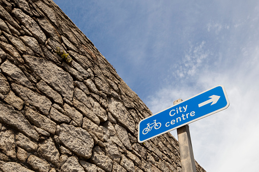 Roadsign indicating the route towards the city centre for cyclists, next to an old stone wall in Liverpool, England