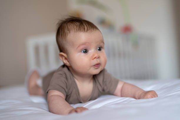 Baby girl crawling on bed Front view of a 3 months old baby girl lying on bed half dressed girls pictures stock pictures, royalty-free photos & images