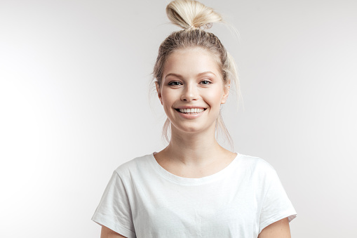 Attractive caucasian cheerful female with blonde hair tied in bun, looking at camera with friendly charming smile over white isolated studio background. People, joy and happiness concept