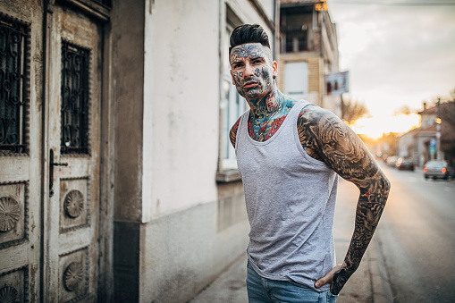 One young modern man with whole body covered in tattoos posing on the street in the city.