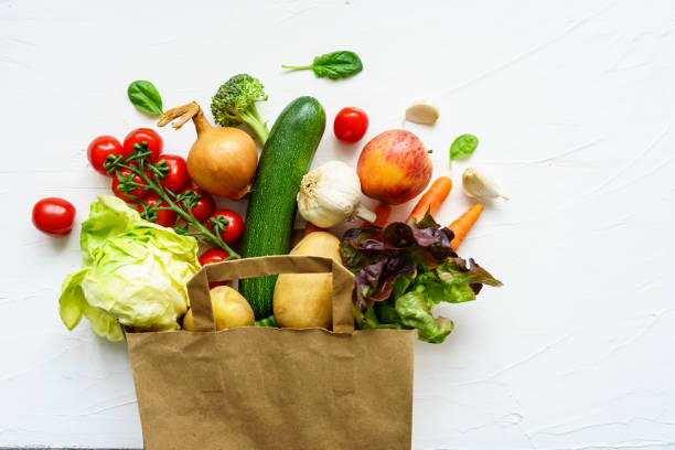 Fresh raw vegetable variation in a paper shopping bag on a white background, top view