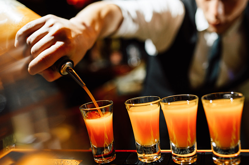 Bartender pouring shots with an orange alcoholic cocktail. close-up