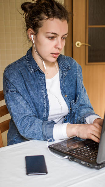 giovane donna concentrata che indossa le cuffie usando il laptop al chiuso. bellissimo lavoro studentesco su gadget per computer, corso audio di ascolto, visione del webinar del seminario di lezione online, apprendimento della lingua. resta a casa. - home schooling audio foto e immagini stock