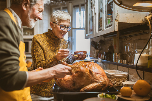 Happy mature couple cooperating while preparing Thanksgiving turkey for dinner in the kitchen. Focus is on woman.