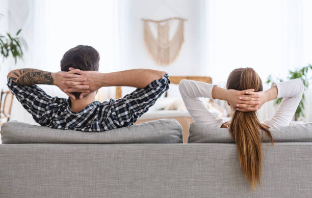 istock Joint rest. Guy and girl relaxing on couch with hands clasped behind head. 1226374587