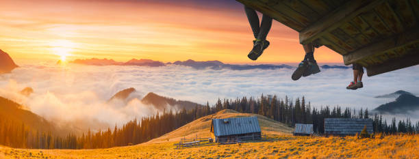Tourists sit on a wooden flooring above the carpathian mountain valley and enjoy golden misty sunset.