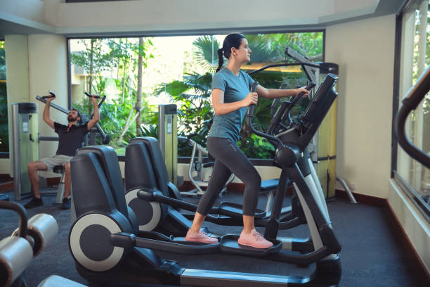 mujer haciendo ejercicio en el gimnasio en un entrenador elíptico. mujer joven haciendo entrenamiento cardiovascular - gym machine smiling coach fotografías e imágenes de stock