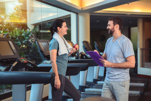 istock Personal trainer working with client in gym. Trainer man giving advises and discussing results with woman in sport club 1226378940