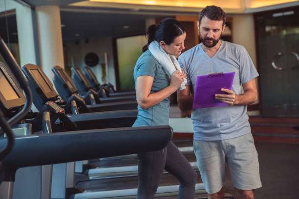 istock Personal trainer working with client in gym. Trainer man giving advises and discussing results with woman in sport club 1226378984