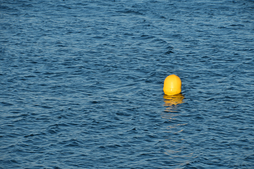 Turquoise blue sea water surface with ripples and waves, yellow floating buoy, high angle view