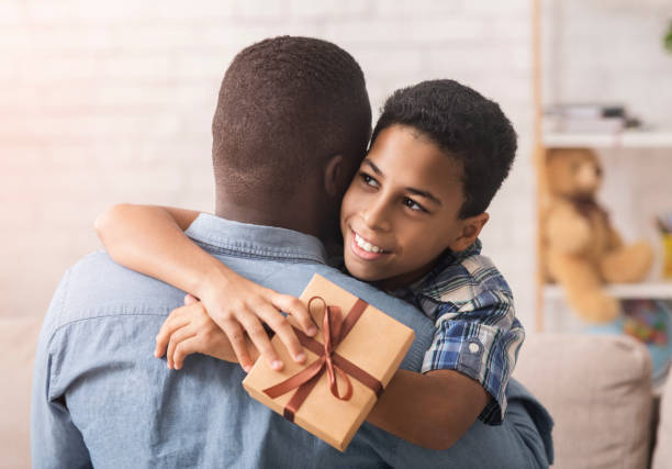 szczęśliwy czarny chłopiec przytulanie tata i dając mu pudełko na prezent - fathers day greeting card father child zdjęcia i obrazy z banku zdjęć