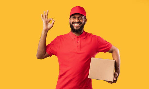 istock Courier Guy Holding Cardboard Box Gesturing Okay On Yellow Background 1226382431