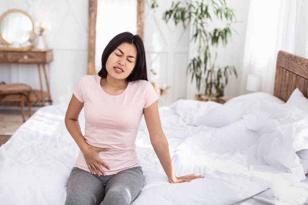 Chinese Girl Having Lower Abdominal Pain Sitting In Bed Indoors Menstrual Cramps. Chinese Girl Having Pelvic Lower Abdominal Pain Having Reproductive Health Problem Sitting In Bed At Home. Copy Space low section stock pictures, royalty-free photos & images