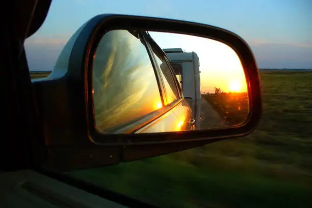 Sunset and trailer reflecting in the car rearview mirror. Caravanning, car traveling, summer holidays concept.