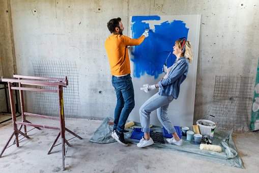 Cheerful couple having fun while painting and decorating their apartment during home renovation process. Copy space.