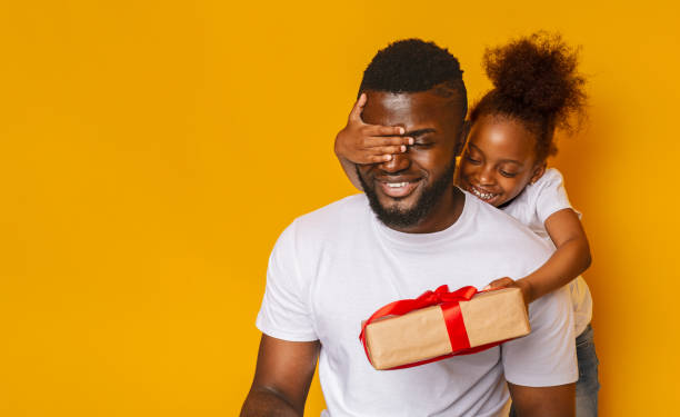 istock Cheerful girl congratulating her daddy, closing his eyes with gift box 1226383794