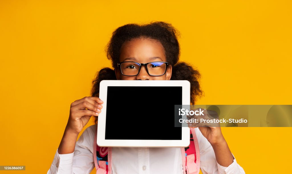 Schoolgirl Holding Digital Tablet With Blank Screen On Yellow Background Online School And E-Learning. Schoolgirl Holding Digital Tablet With Blank Screen Recomending Web Classes And Distant Learning On Yellow Background. Child Stock Photo