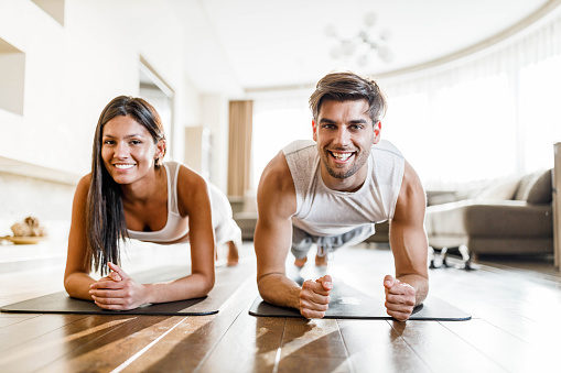 Young athletic couple exercising endurance in a plank position at home and looking at camera. Copy space.