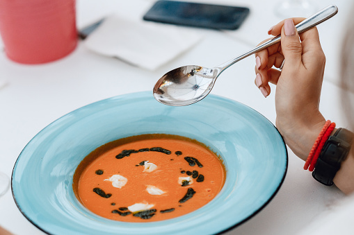 Girl eating Spanish gazpacho soup in a restaurant. Close-up of a hand with a spoon and a plate
