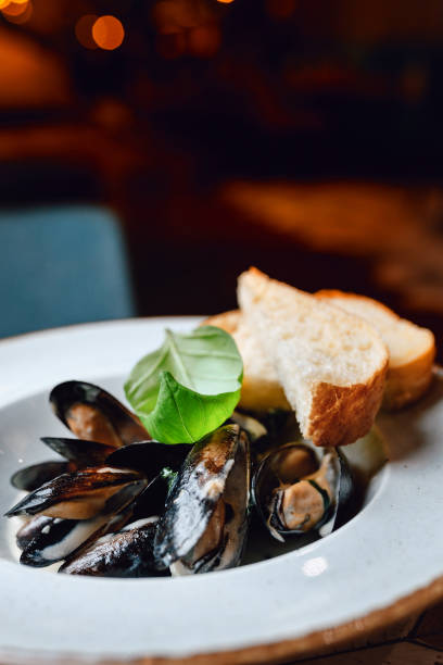 istock White plate with mussels decorated with a basil on a table in a restaurant. Different focus, blurry lights in the background 1226399566