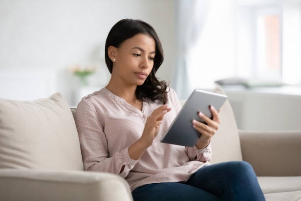 African woman sit on couch using tablet gadget