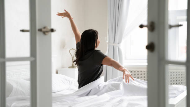 femme de rétroviseur réveillé étiré ses sourires de bras apprécient le nouveau jour - hotel room hotel luxury mattress photos et images de collection