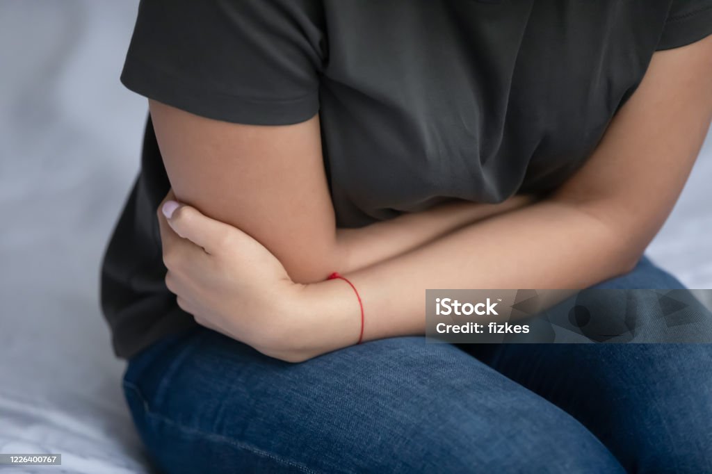 Closeup image woman sitting in bed feeling stomach ache Close up view young woman sit in bed curled up in pain feeling stomachache caused by indigestion, gallstones or painful menstrual period. Gas, appendicitis, ulcers, gastritis need treatment concept Miscarriage Stock Photo