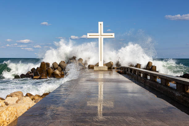 Waves are breaking into thousands of splashes on a pier with a cross mounted on it. The picture was taken in Bulgaria at the resort of Saints Constantine and Helena.