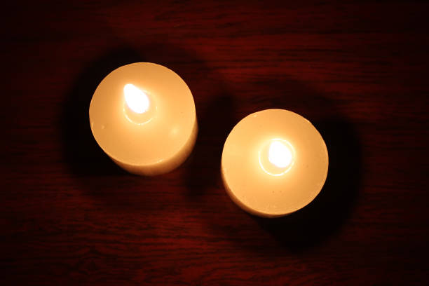 Top view of two white burning candles on the red wood background