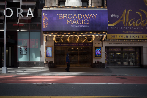 May 20, 2020. Manhattan, New York, Usa. A man wearing a mask walks in front of the empty entrance of the New Amsterdam Theatre on 42nd street featuring the Broadway show \